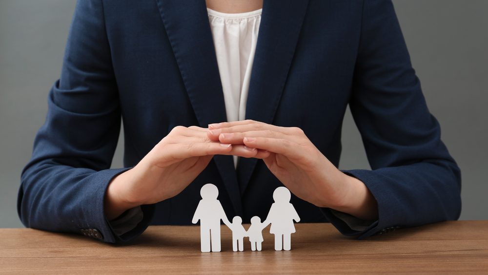 Hands sheltering a paper cut out of a family